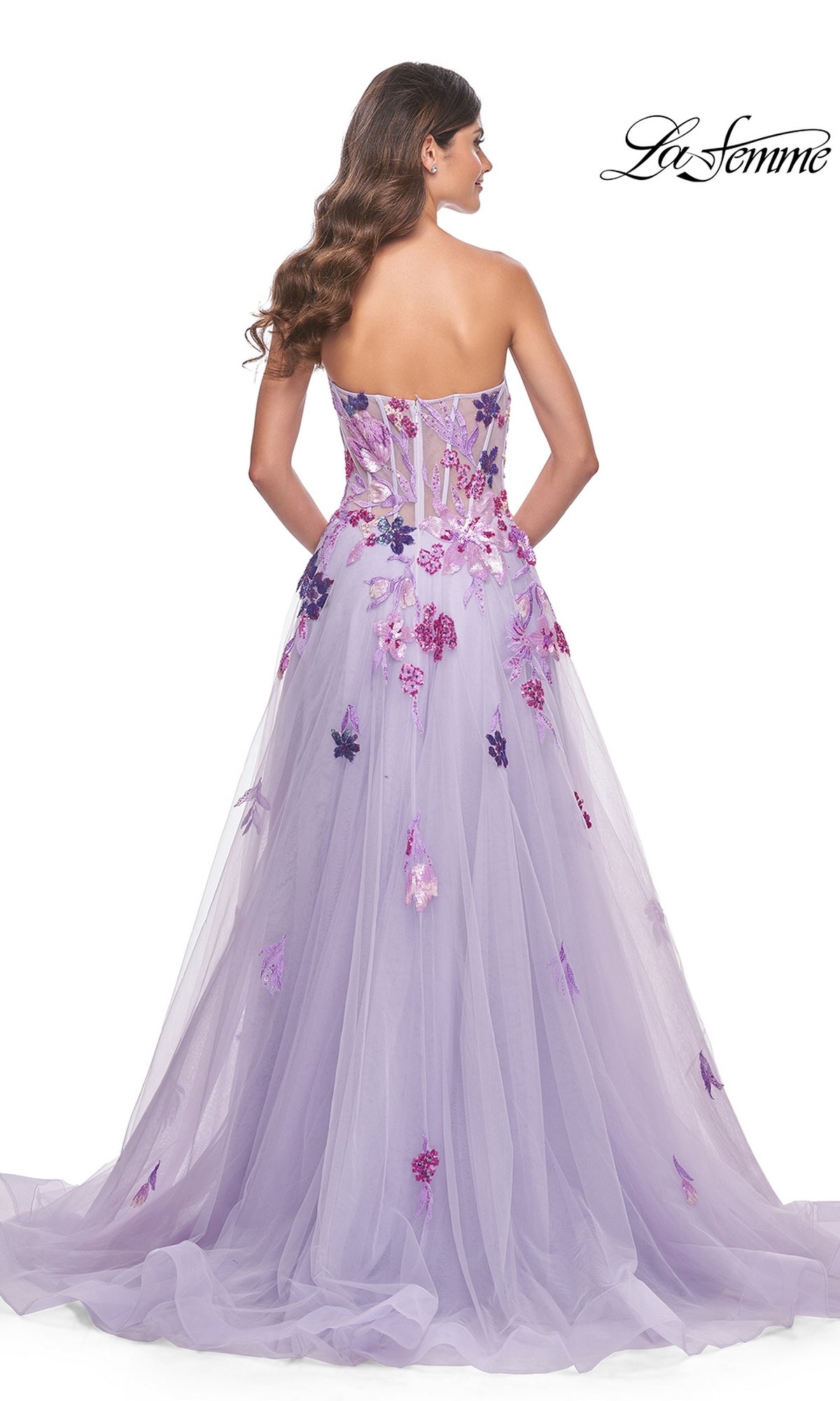 A woman faces away, showcasing the La Femme Strapless Long Lavender Prom Dress 32156 with floral appliqués, a sheer bodice, and a flowing tulle A-line skirt.